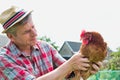 Photo of mature farmer wearing hat while carrying hen at barn Royalty Free Stock Photo