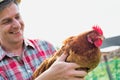 Photo of mature farmer wearing hat while carrying hen at barn