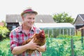 Photo of mature farmer wearing hat while carrying hen at barn Royalty Free Stock Photo