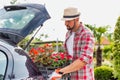 Portrait of mature gardener putting flowers on crate in car trunk for delivery