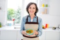 Photo of mature sweet lady hold soup wear apron jeans shirt at kitchen alone Royalty Free Stock Photo