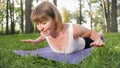 Photo of middle aged smiling woman practicing yoga and meditating at park. Woman stretching and doing fitness on mat at Royalty Free Stock Photo