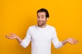 Photo of millennial unsure brunet guy shrug shoulders wear white shirt isolated on bright yellow color background