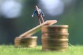 Miniature figure young bussinesman keep trying to get higher income walking at stack of coin at fresh green grass in the morning Royalty Free Stock Photo