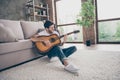 Photo of mixed race guy sitting floor leaning sofa hold acoustic instrumental guitar playing new written song sound