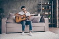 Photo of mixed race guy sitting sofa hold acoustic instrumental guitar playing new written song sound love his hobby