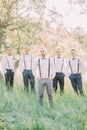 The photo of the modern-dressed groom and his best men in the green spring field.