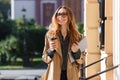 Photo of modern woman 20s drinking takeaway coffee while walking through city street