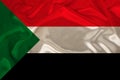 Photo of the national flag of Sudan on a luxurious texture of satin, silk with waves, folds and highlights, close-up, copy space,