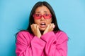 Photo of nervous scared Asian woman dressed in pink jacket and glasses grabs face and looks with worried expression she