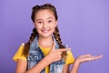 Photo of nice little blond girl hold index empty space wear yellow t-shirt jeans vest isolated on violet color Royalty Free Stock Photo