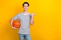 Photo of nice student dressed striped t-shirt hold bascketball ball indicating at offer empty space isolated on yellow