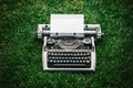 Photo of old typewriter on a green grass with a sheet of paper.