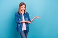 Photo of optimistic teen blond girl show empty space wear jeans shirt isolated on blue color background Royalty Free Stock Photo