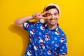 Photo of optimistic young guy showing v sign cover face peace symbol wear blue cool santa claus shirt isolated on yellow Royalty Free Stock Photo