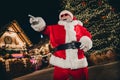 Photo of overjoyed cheerful aged santa pointing finger laughing magic atmosphere city center garland lights outside