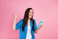 Photo of overjoyed cute girl dressed blue shirt look at smartphone win lottery shout yeah hold fist up isolated on pink Royalty Free Stock Photo