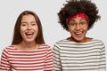 Photo of overjoyed mixed race women wear striped jumpers, laugh at good joke, gaze at camera with satisfied expressions