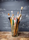 Photo of paint brushes in a glass standing on old wooden table,