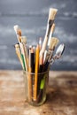 Photo of paint brushes in a glass standing on old wooden table,