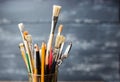 Photo of paint brushes in a glass standing on old wooden table,