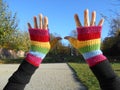 pair of hands wearing a rainbow colored hand made crochet fingerless gloves