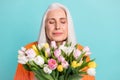 Photo of peaceful charming elderly woman smell flowers tulips wear orange sweater isolated on teal color background Royalty Free Stock Photo