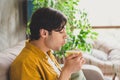 Photo of peaceful handsome guy hold mug enjoy warm cacao beverage blow lips wear yellow shirt home indoors