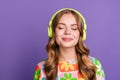 Photo of peaceful relaxed woman with wavy hair wear stylish t-shirt listen calm music in headphones isolated on purple