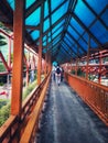 photo of a pedestrian bridge, long hallway, with orange railings and a blue roof in the buffer city of Jakarta