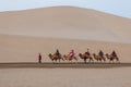 Photo of people riding on camels in a desert landscape