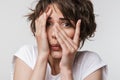 Photo of perplexed woman with short brown hair in basic t-shirt keeping hand over her face and looking at camera