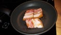 Photo pieces of bacon are fried in a black frying pan
