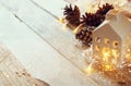 Photo of pine cones and decorative wooden house next to gold garland lights on wooden background. copy space. retro filtered