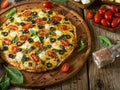 In the photo - pizza on a round wooden dish. Beautiful ruddy crust. Tomatoes, olives, mint leaves. In the background are tomatoes Royalty Free Stock Photo