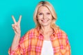 Photo of pleasant nice woman with straight hairstyle dressed checkered shirt showing v-sign symbol isolated on teal Royalty Free Stock Photo