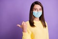 Photo Portrait Of Attractive Girl Pointing Thumb Behind Blank Space Wear Facial Safety Flu Mask Isolated Purple Colored