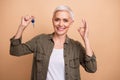 Photo portrait of attractive retired woman hold key show okey symbol dressed stylish khaki clothes isolated on beige Royalty Free Stock Photo