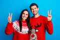 Photo portrait of attractive young couple showing v-sign showing dressed x-mas ornament red sweaters isolated on blue Royalty Free Stock Photo