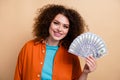 Photo portrait of attractive young woman hold money banknotes fan dressed stylish orange clothes isolated on beige color Royalty Free Stock Photo