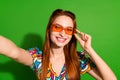 Photo portrait of attractive young woman sunglass selfie photo dressed stylish retro clothes isolated on green color Royalty Free Stock Photo