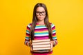 Photo portrait of calm serious schoolgirl keeping pile of books for studying wearing spectacles isolated vibrant yellow