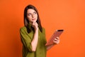 Photo portrait of dreamy brunette student thinking about idea keeping tablet isolated on bright orange color background