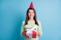 Photo portrait of excited girl holding red present wearing cone isolated on pastel blue colored background