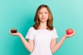 Photo portrait girl comparing sweet cupcake apple unsure sad isolated bright teal color background Royalty Free Stock Photo