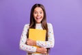 Photo portrait of happy amazed schoolgirl hugging yellow book preparing for lesson smiling isolated on bright purple