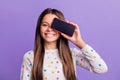 Photo portrait of happy girl covering one eye with phone with blank space isolated on bright purple colored background Royalty Free Stock Photo