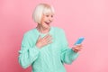 Photo portrait of happy laughing grandmother reading information on cellphone hand on chest isolated on pastel pink