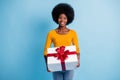 Photo portrait of happy smiling black skinned woman holding wrapped with red ribbon gift isolated on vibrant blue color