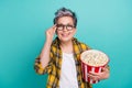 Photo portrait of lovely senior lady hold popcorn bucket touch specs wear trendy plaid yellow garment isolated on cyan